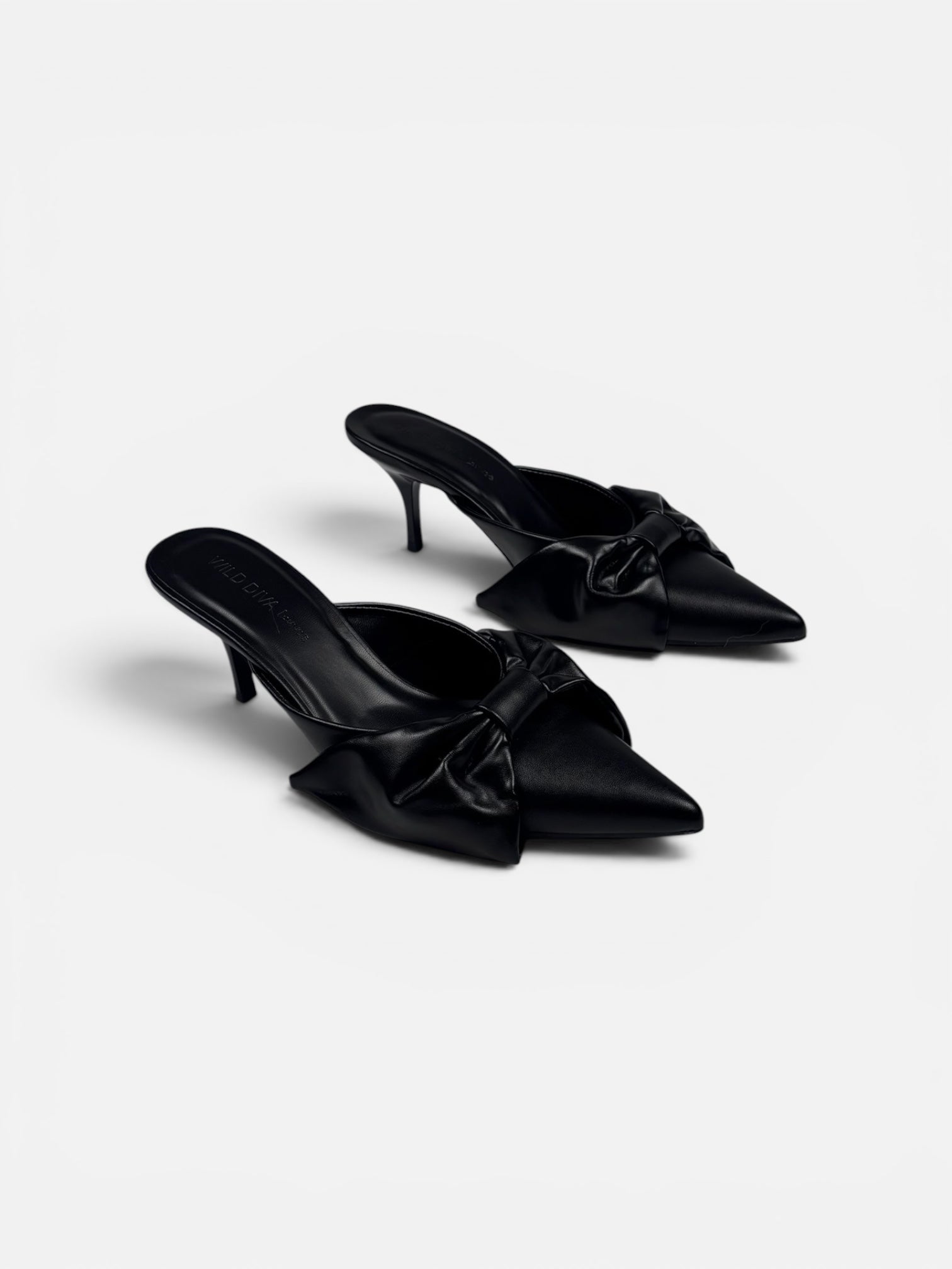 Pair of black satin mules with bow details on a white background