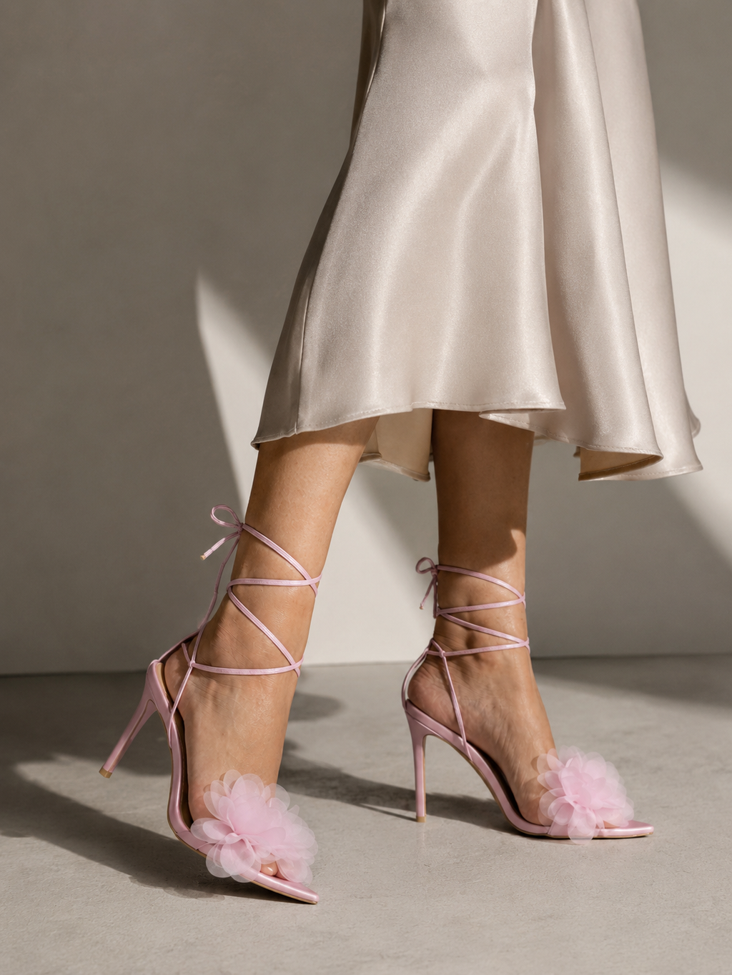 Woman walking in a satin dress wearing pink lace-up stiletto sandals with a chiffon flower detail