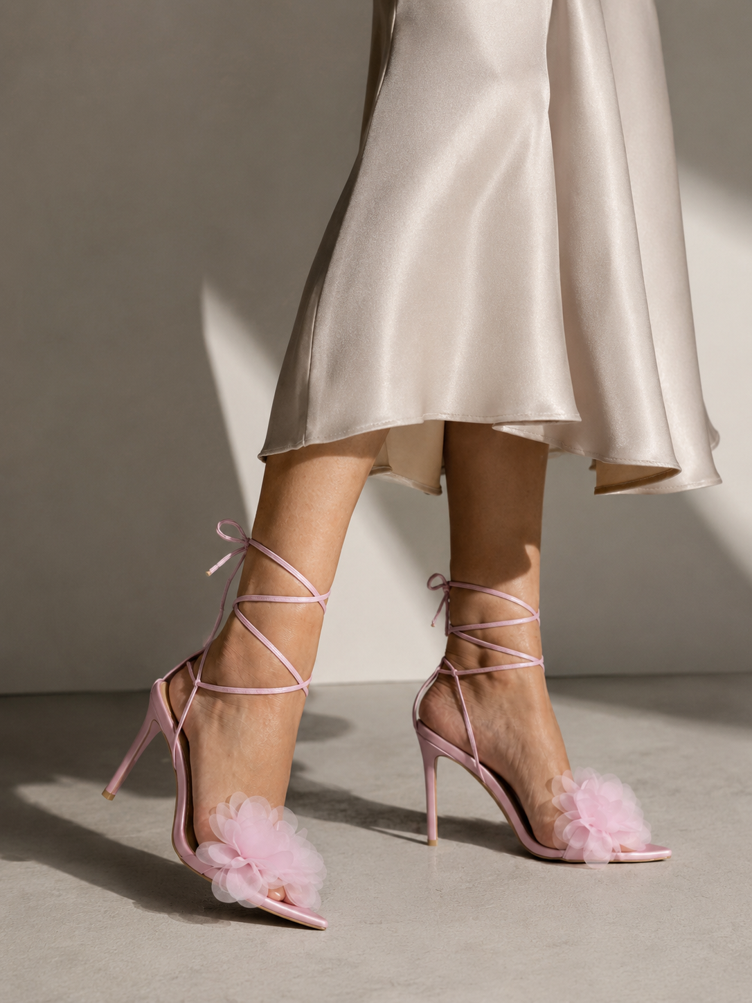 Woman walking in a satin dress wearing pink lace-up stiletto sandals with a chiffon flower detail