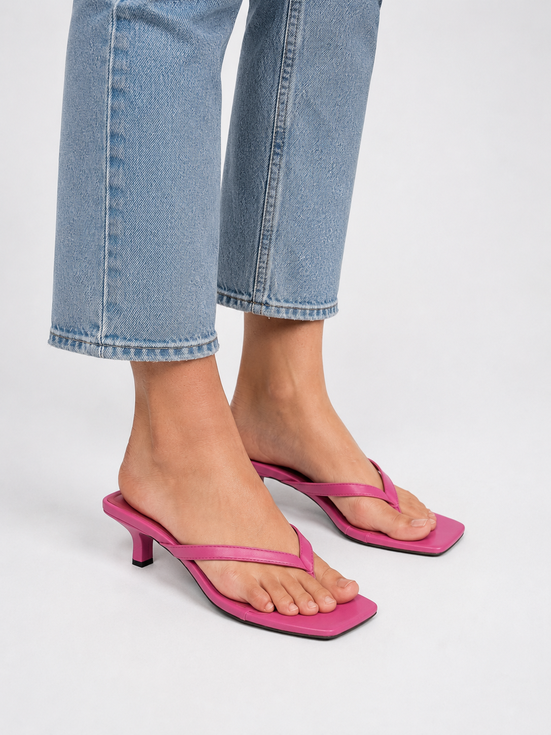 Close-up of pink thong sandals worn with cropped jeans
