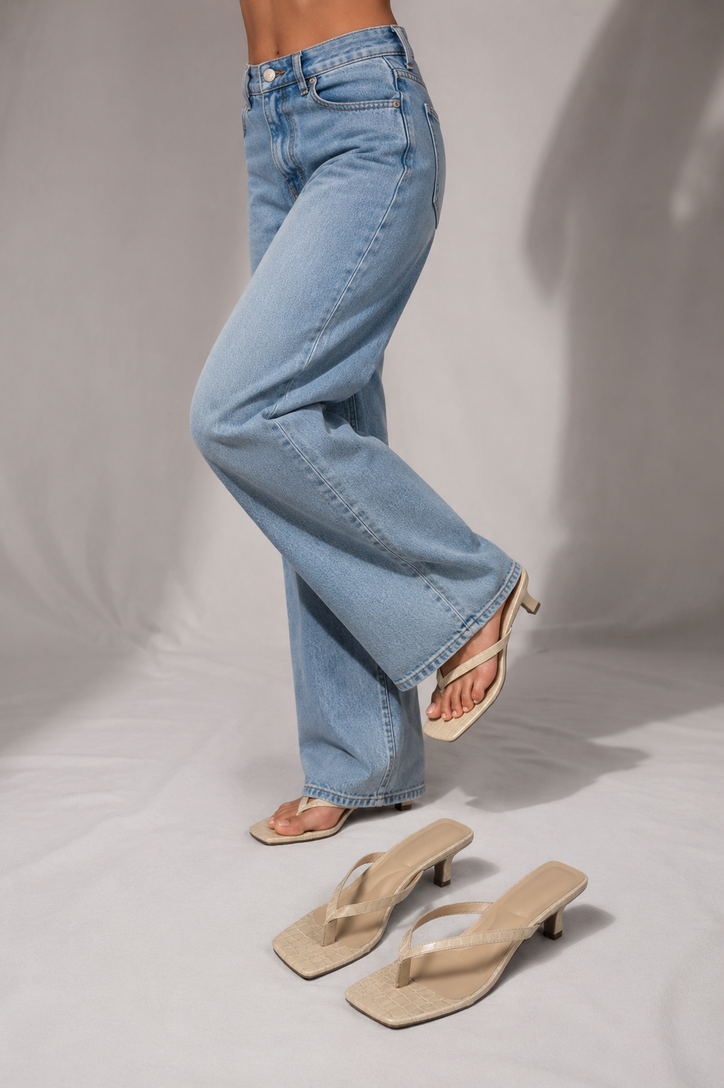 Woman in wide-leg jeans stepping barefoot next to a pair of ivory croc-embossed thong sandals